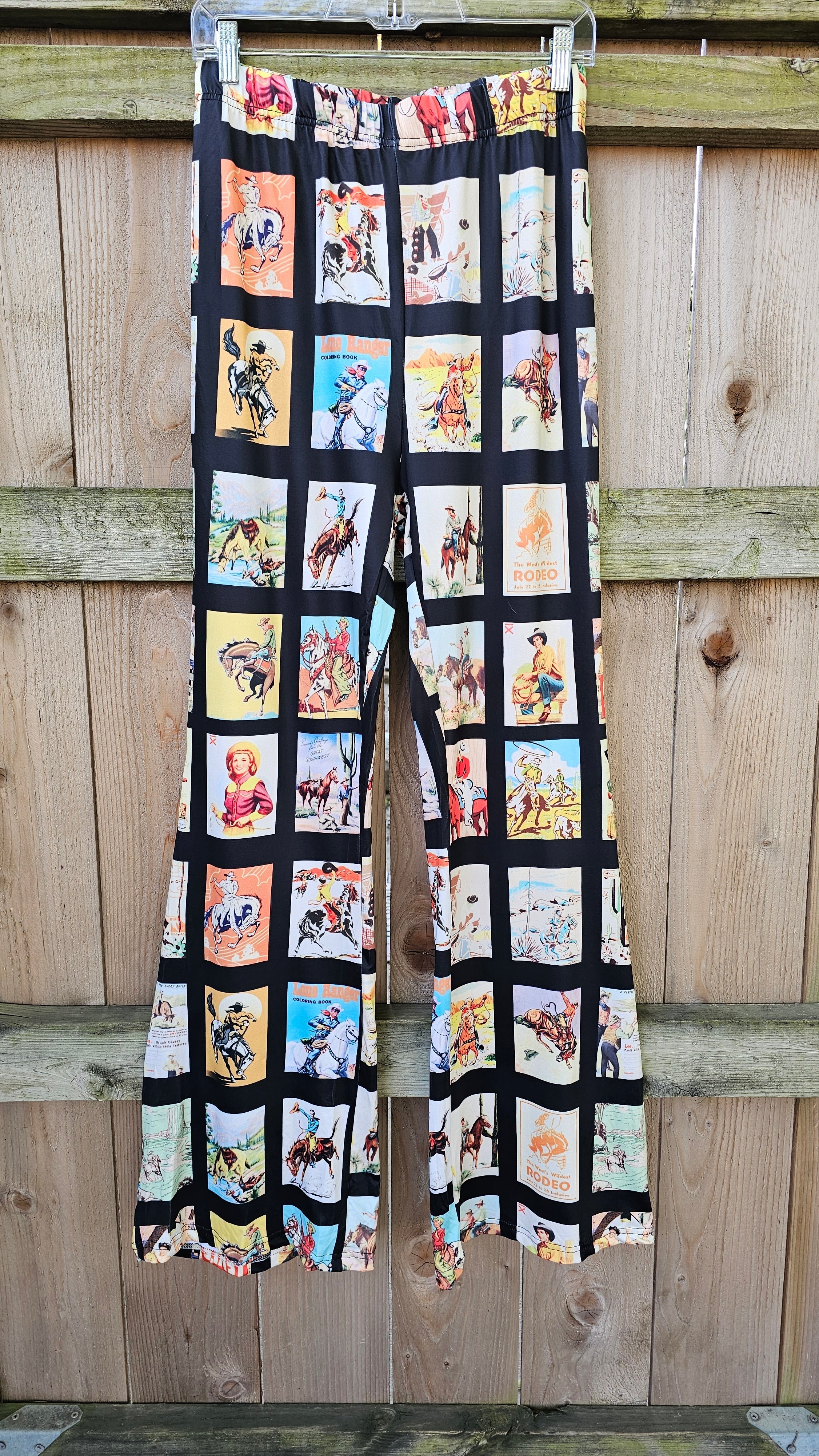 Vintage Cowboy Collage Western Flare Pants showcasing retro rodeo designs and dramatic flares on a wooden backdrop.