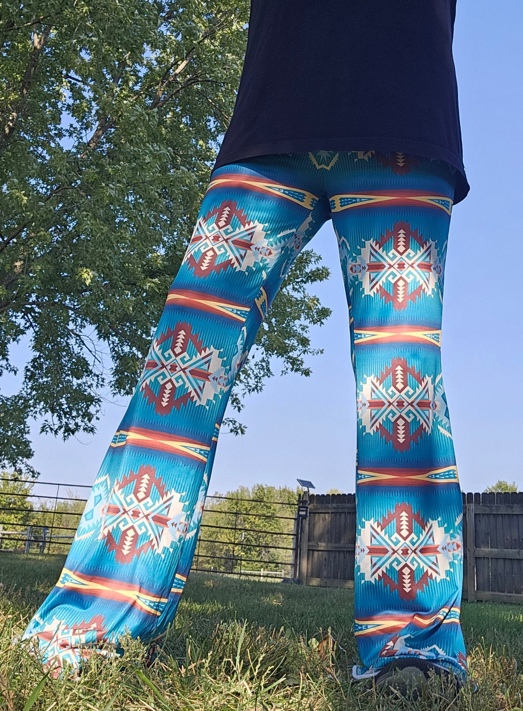 Model wearing teal Aztec flare pants in a grassy outdoor setting, showcasing vibrant southwestern design.