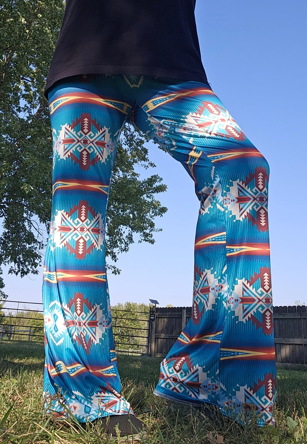 Vibrant teal Aztec flare pants on display outdoors, featuring a bold southwestern pattern against a clear sky.