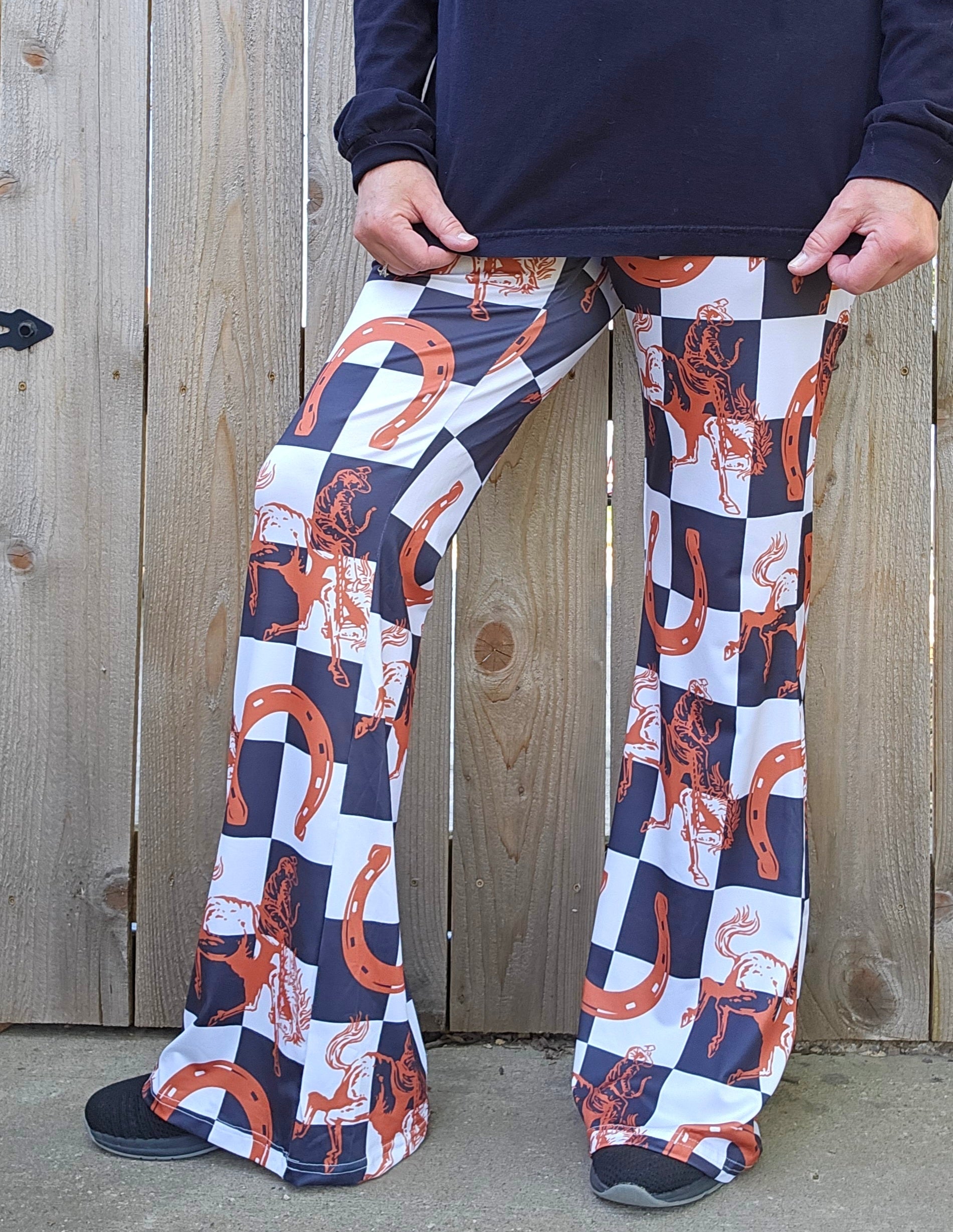 Model wearing Checkered Rodeo Flare Pants with Western print, showcasing stylish high-waisted design against a wooden background.