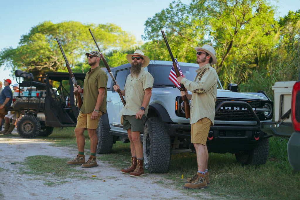 Three men in outdoor gear holding rifles, standing by a truck in a natural setting, perfect for adventure enthusiasts.