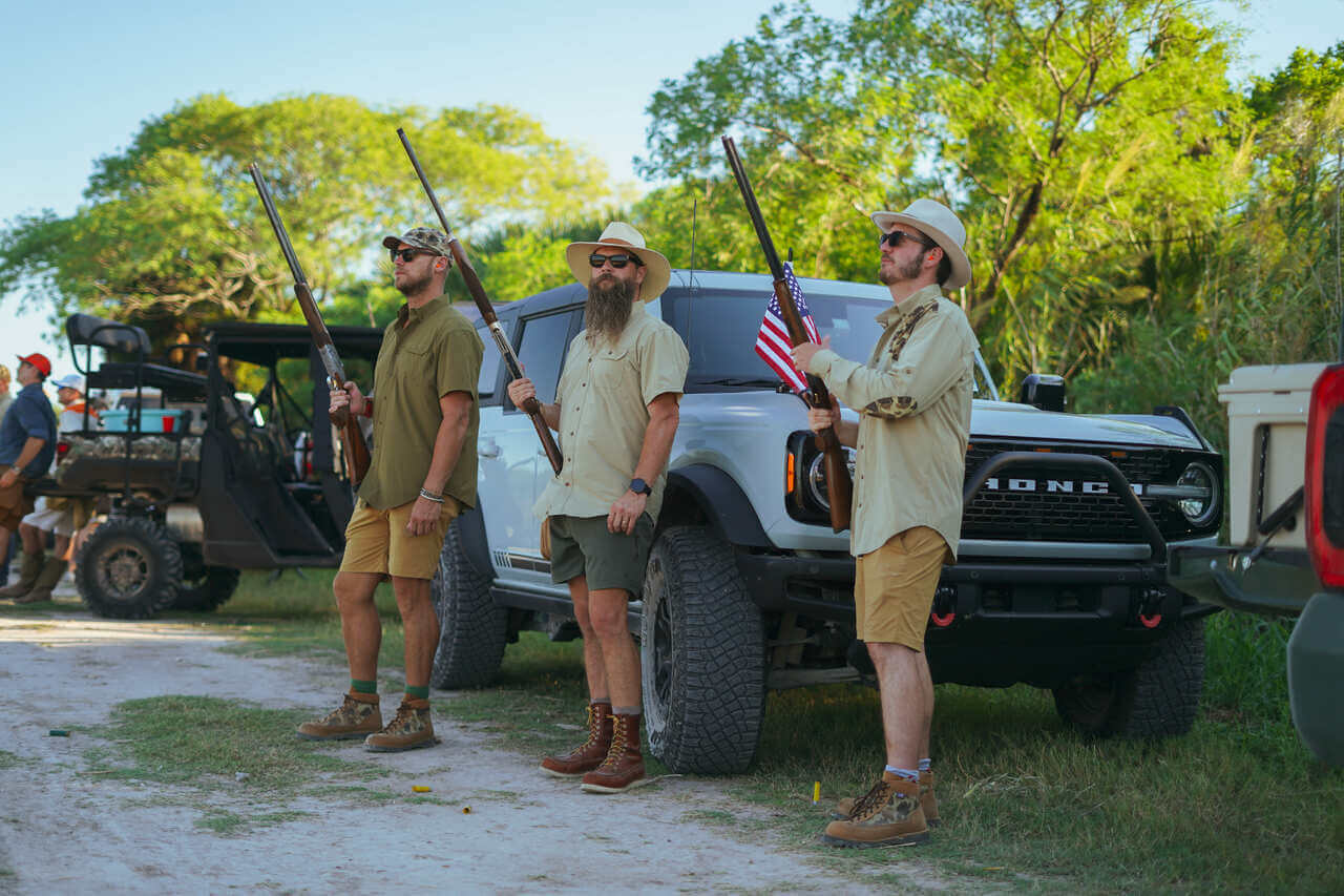 Three men in outdoor gear holding rifles, standing by a truck in a natural setting, perfect for adventure enthusiasts.