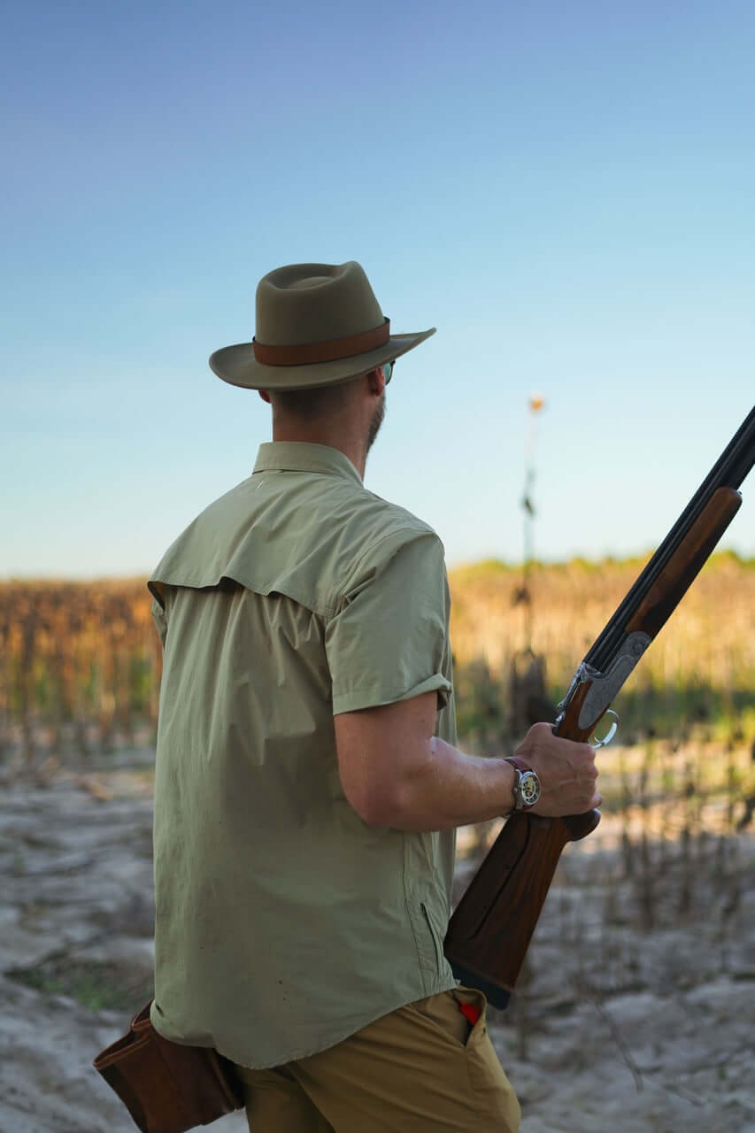 Man wearing a Brimmed Field Hat in felted wool, holding a rifle in a serene outdoor setting.