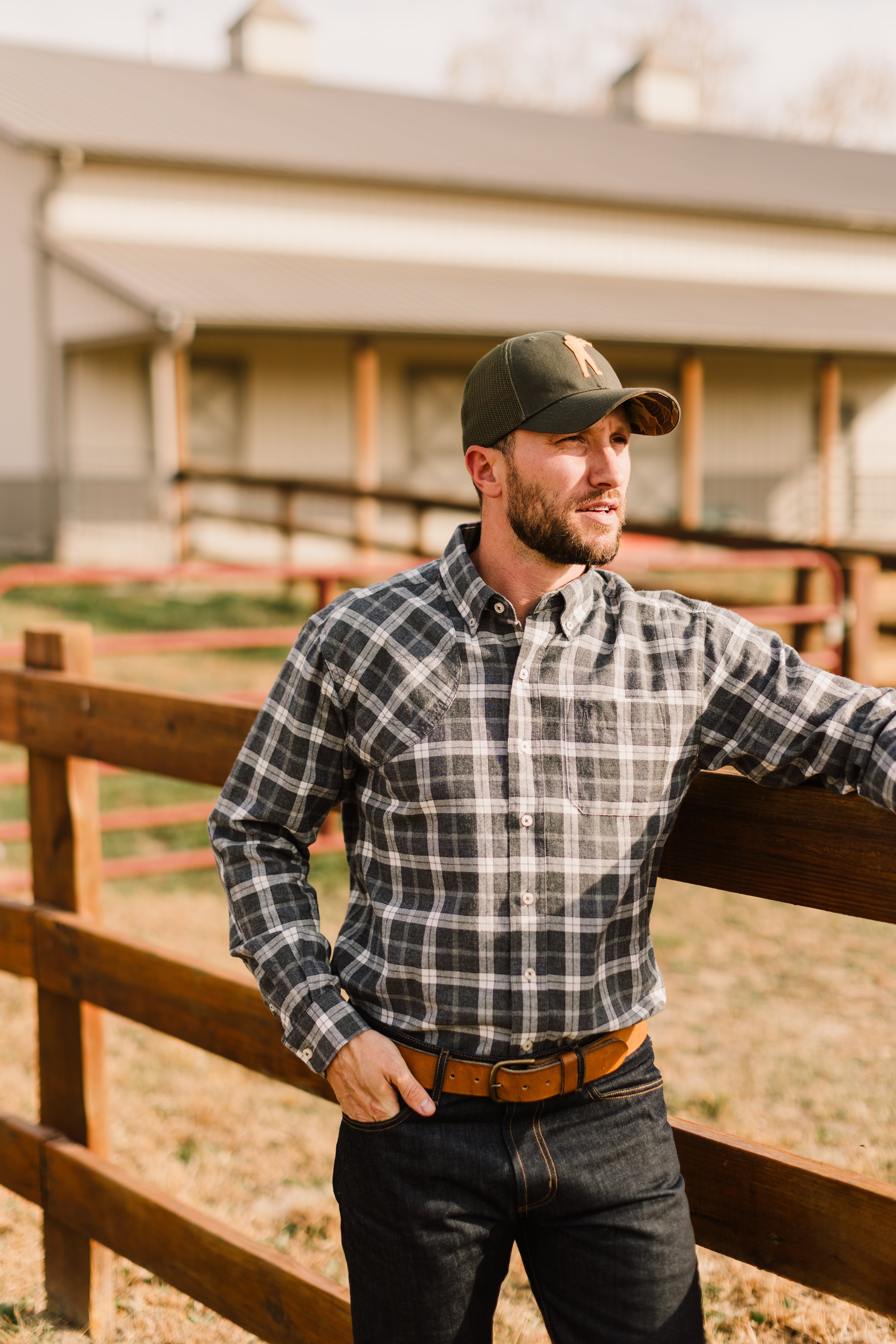 Man wearing Arthur Core Snapback Hat and plaid shirt, standing by a wooden fence, embodying a sporty lifestyle.