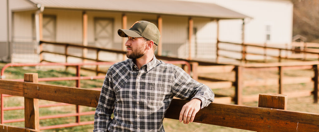 Man wearing Arthur Core Snapback Hat, standing by a wooden fence in a rustic setting, showcasing a sporty lifestyle.