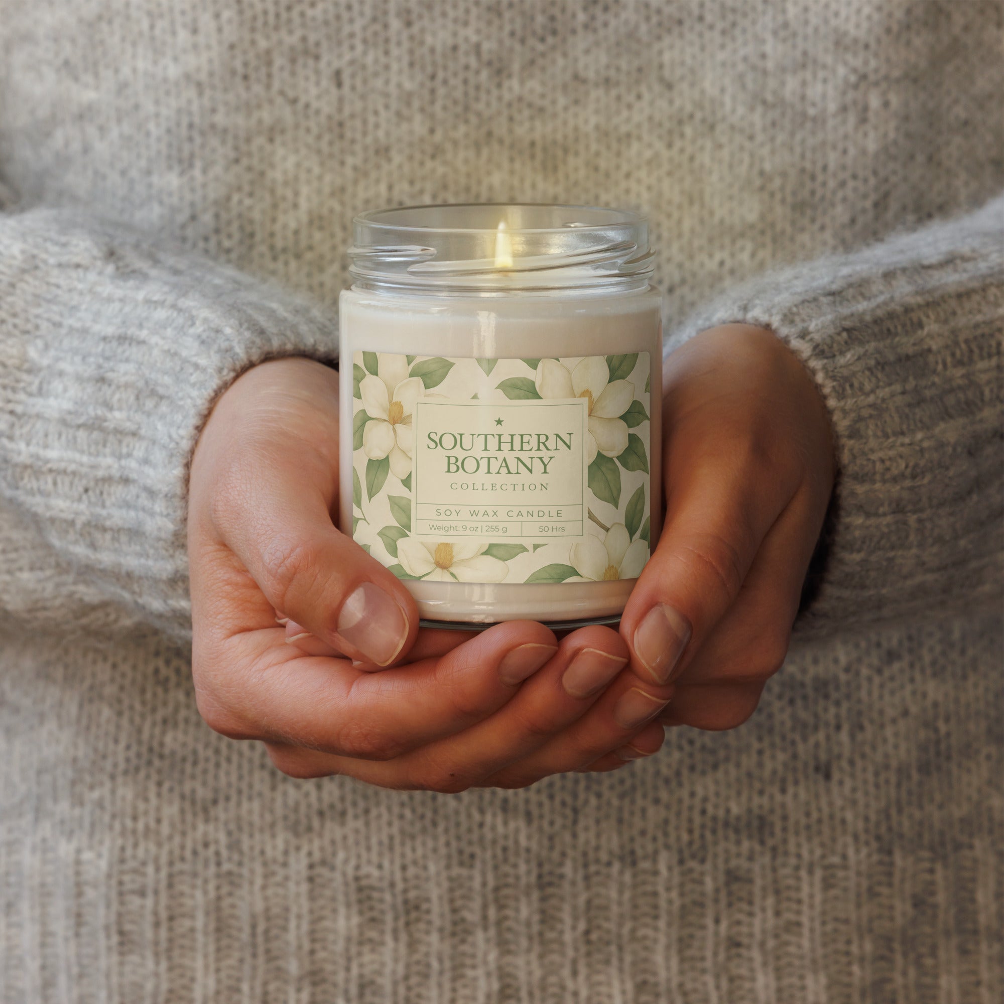 Person holding a Magnolia candle from Southern Botany Collection with floral design in a cozy setting.
