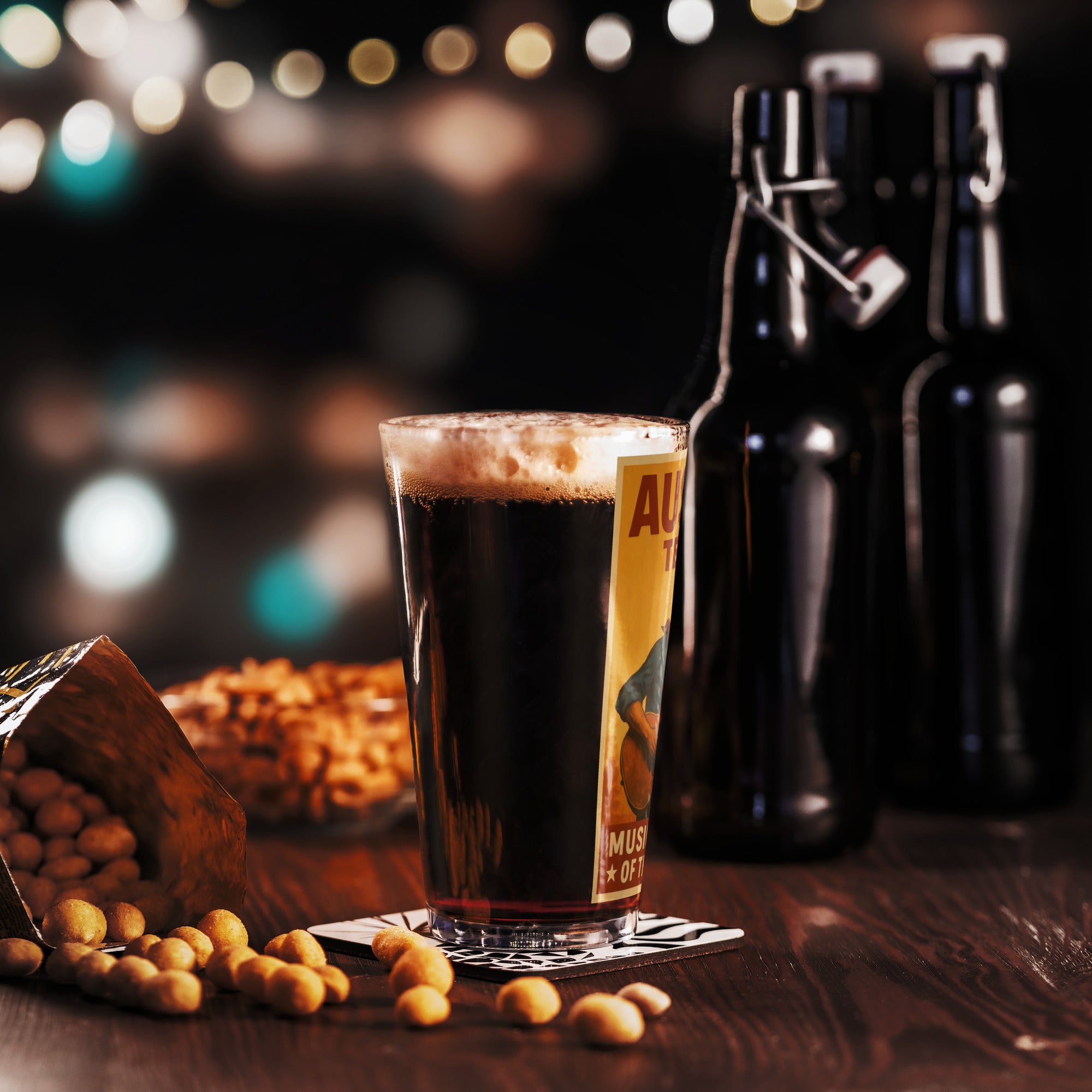 Vintage Austin, Texas pint glass filled with dark beer, surrounded by snacks and beer bottles, on a wooden table.