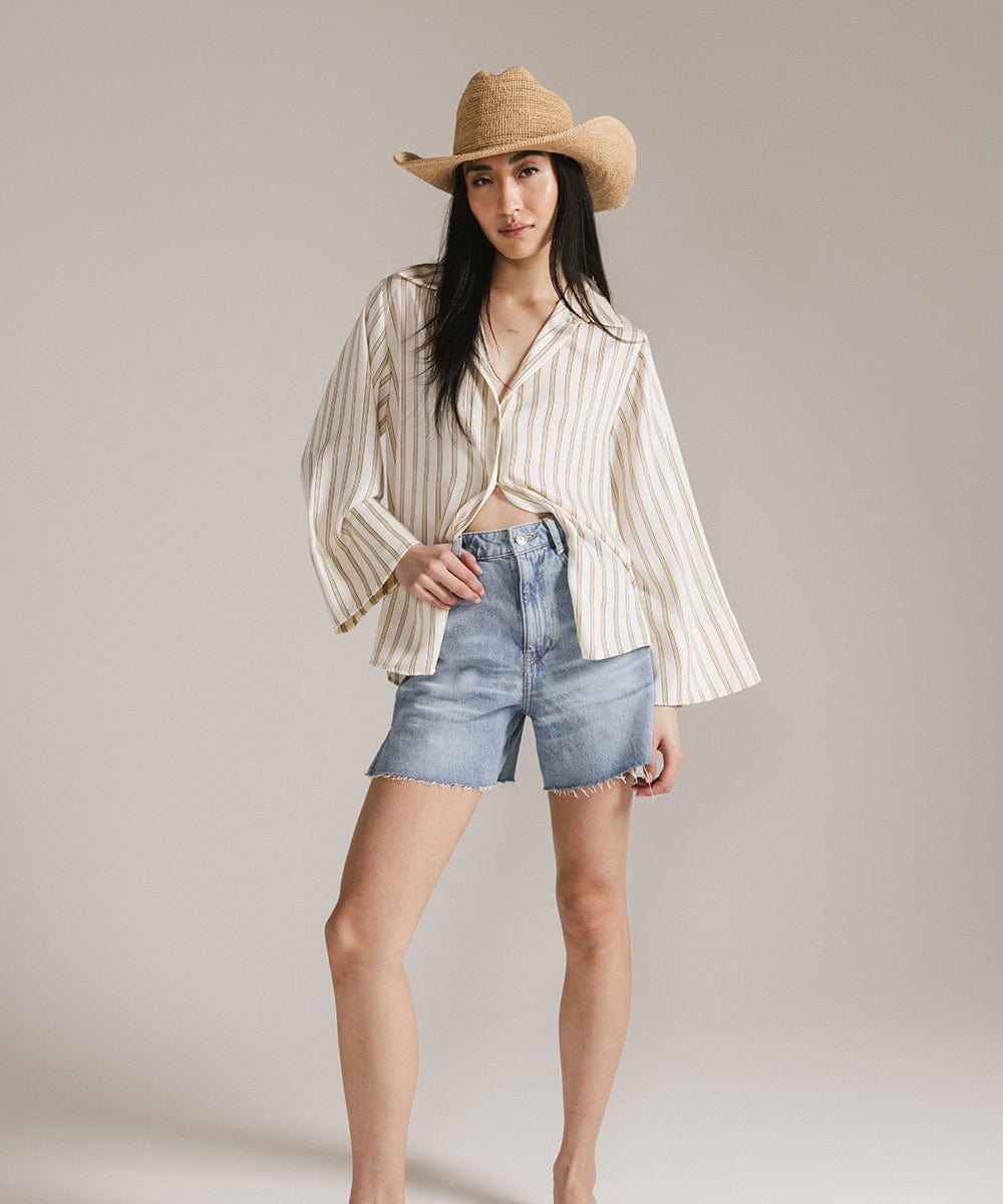 Woman wearing an Ames packable straw cowboy hat with a striped shirt and denim shorts, showcasing a Western-inspired look.