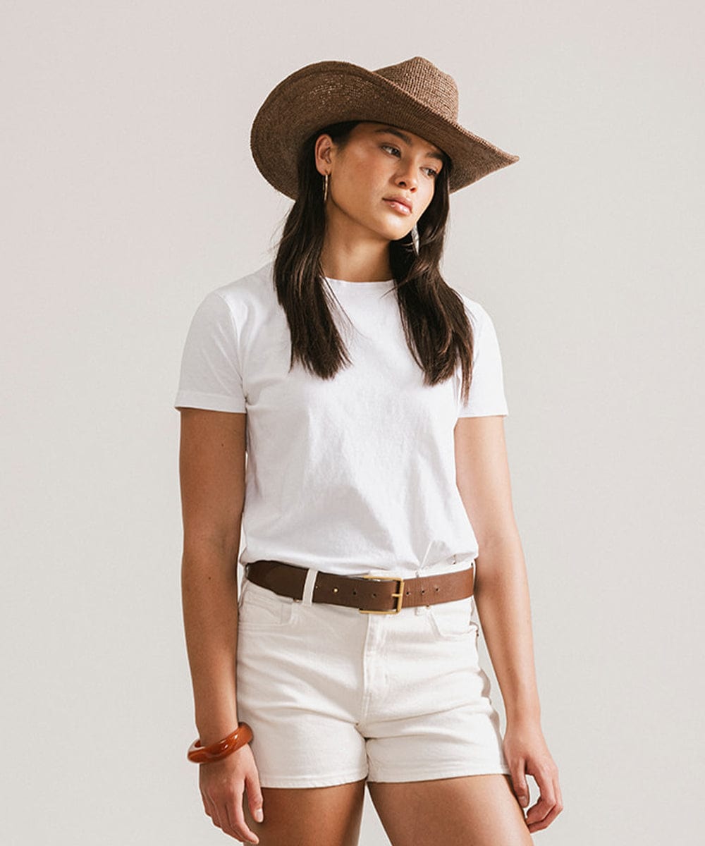 Woman wearing a straw cowboy hat showcasing a casual Western style with a white t-shirt and shorts.